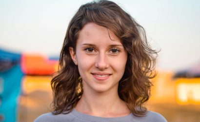 Young woman smiling outdoors with blurred background.
