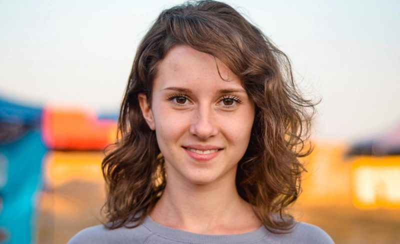 Young woman smiling outdoors with blurred background.