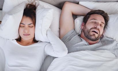 A man snoring loudly while a woman covers her ears in bed.