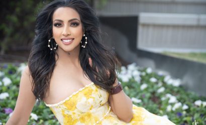 Woman in a yellow floral dress smiling outdoors.