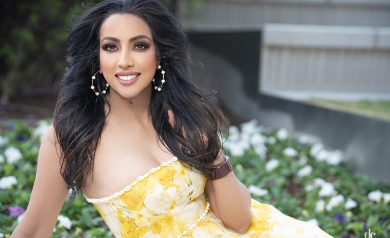Woman in a yellow floral dress smiling outdoors.